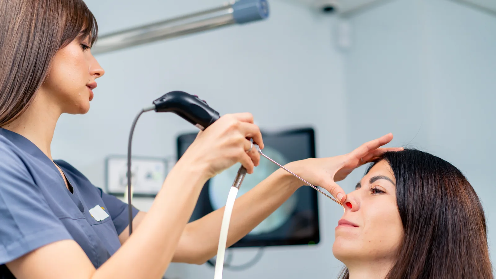 Profissional realizando endoscopia nasal em uma paciente, com o endoscópio conectado ao monitor do consultório.
